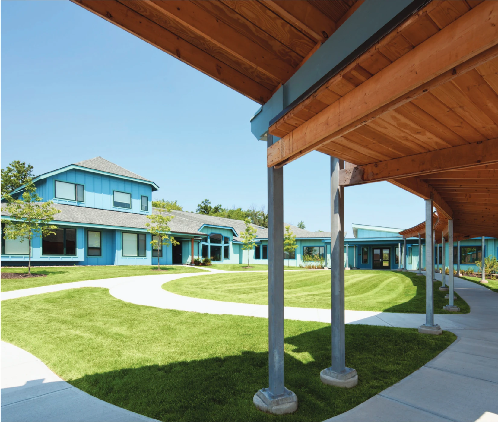 Timber-covered walkway and blue residential buildings at Camphill Ghent
